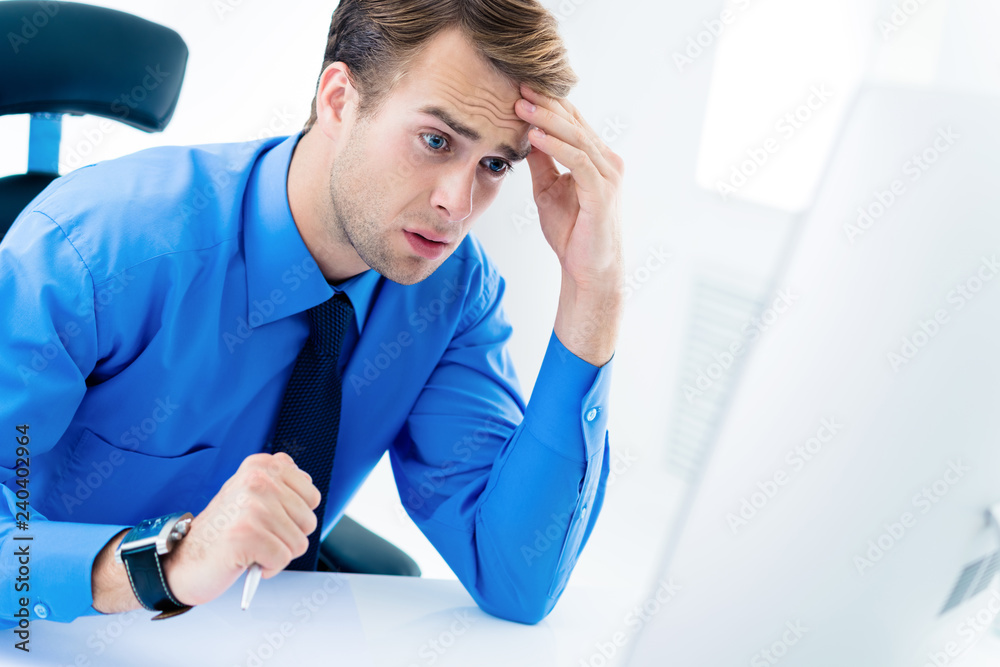 Shocked or surprised unhappy businessman in confident blue shirt and glasses, working with desktop computer at office. Business, job and education concept. Shocked or surprised unhappy businessman in confident blue shirt and glasses, working with desktop computer at office. Business, job and education concept.