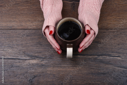Female hands with a manicure hold a cup of coffee on a wooden background