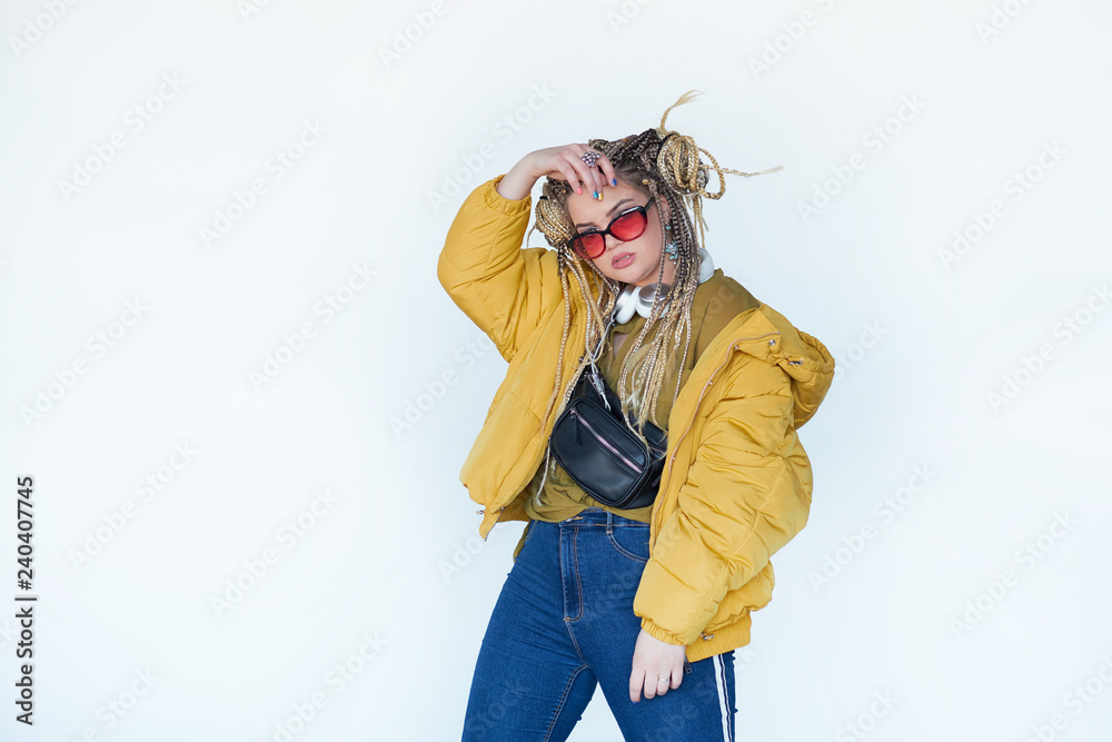 young blonde girl in sunglasses with african pigtails listens to music in headphones and dances against a white background. young blonde girl in sunglasses with african pigtails listens to music in headphones and dances against a white background.