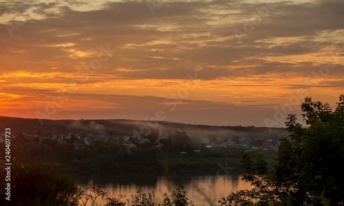 Fototapeta Naklejka Na Ścianę i Meble -  Dawn over the river. Sunrise over the village. Morning rays of the sun. The first rays of the rising sun. The village is at dawn. Smoke from the pipes of houses. Summer sky in the morning. The village