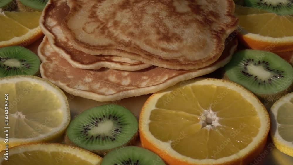 Rotation of batter cake pile among kiwifruit and orange slices on dark grey plate with up center close up. Appetizing natural food background with amazing texture. Home eating side view. Rotation of batter cake pile among kiwifruit and orange slices on dark grey plate with up center close up. Appetizing natural food background with amazing texture. Home eating side view.