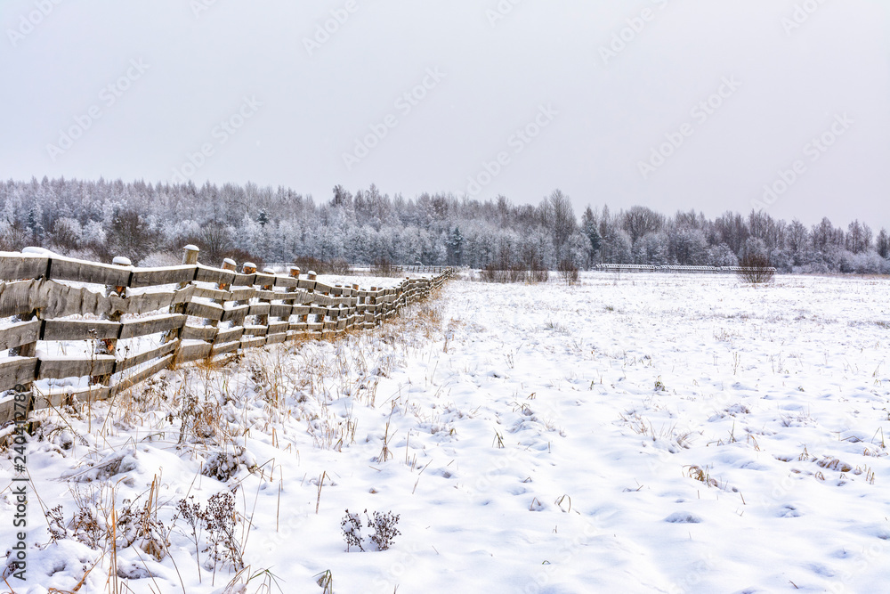 Snow-covered field in the countryside. A wooden fence of farmland. Snow-covered field in the countryside. A wooden fence of farmland.
