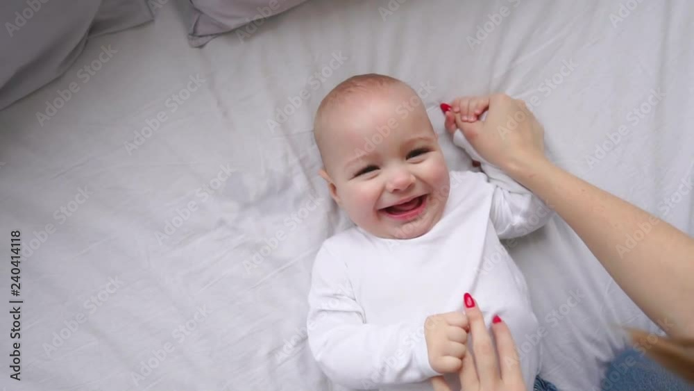 Baby in white t-shirt lying on a white bed and laughing looking at the camera top view slow motion Baby in white t-shirt lying on a white bed and laughing looking at the camera top view slow motion