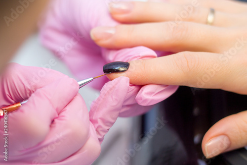 Nail Care And Manicure concept. Closeup Manicurist hands in pink gloves is Painting black Nail Polish On Client s Nails. Woman In Beauty Salon.