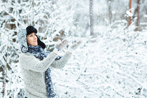 Fototapeta Naklejka Na Ścianę i Meble -  Beautiful girl plays with falling snow in the winter forest