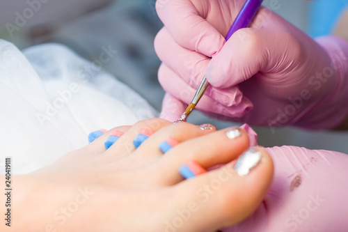 Nail Care And pedicure concept. Closeup Manicurist hands in pink gloves is Painting gold Nail Polish On Client's toes. Woman In Beauty Salon.
