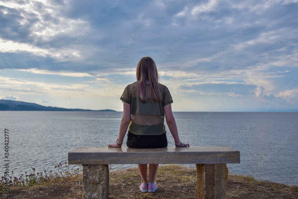 girl sitting on a bench near the sea and looking into the distance