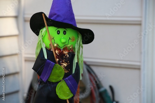 Green Felt Witch Halloween Decoration with Black Eyes Wood Broom Blue Cape and Hat with Shiny Bronze Ruffles against White Wall of Victorian-Style Townhome in Burke, Virginia photo