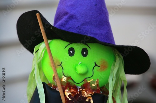 Green Felt Witch Halloween Decoration with Black Eyes Wood Broom Blue Cape and Hat with Shiny Bronze Ruffles against White Wall of Victorian-Style Townhome in Burke, Virginia photo