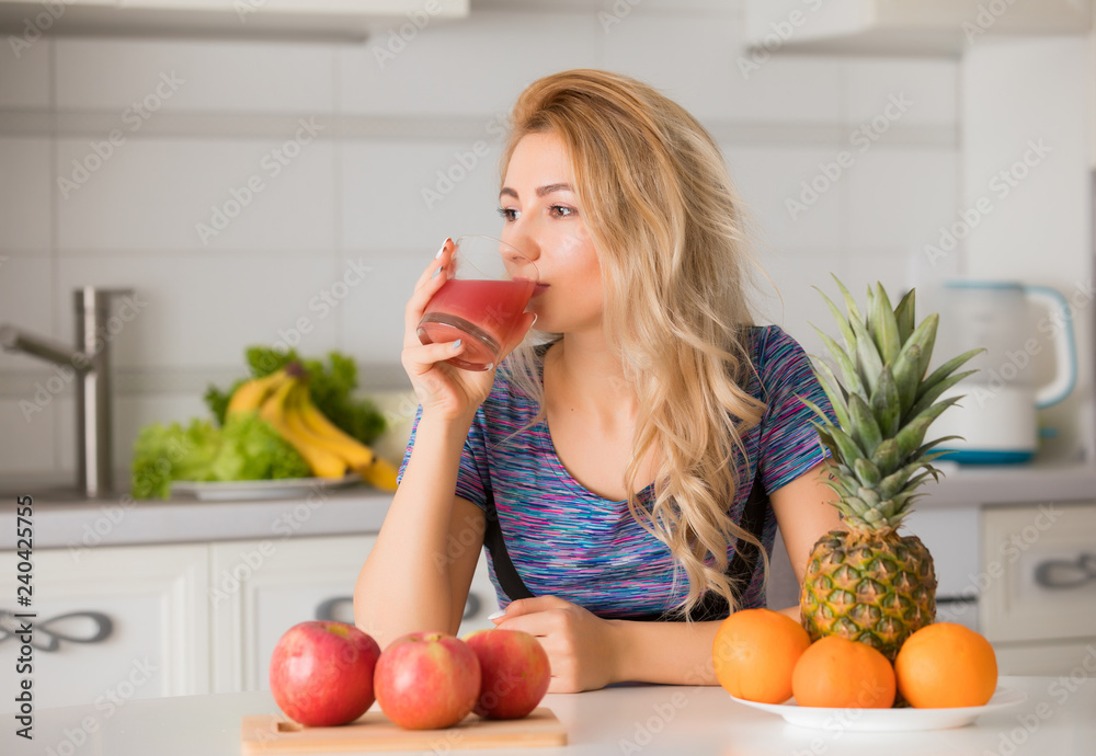 Pretty woman drinking juice on kitchen, fruits on a table, healthy lifestyle Pretty woman drinking juice on kitchen, fruits on a table, healthy lifestyle
