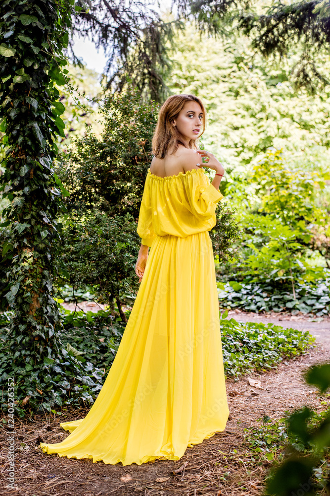 A girl in a long yellow dress is dancing in the open air