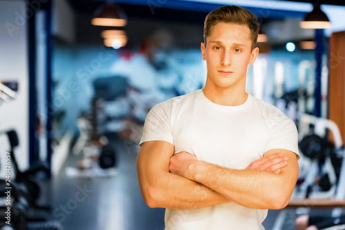 Young handsome fitness trainer sits modern gym