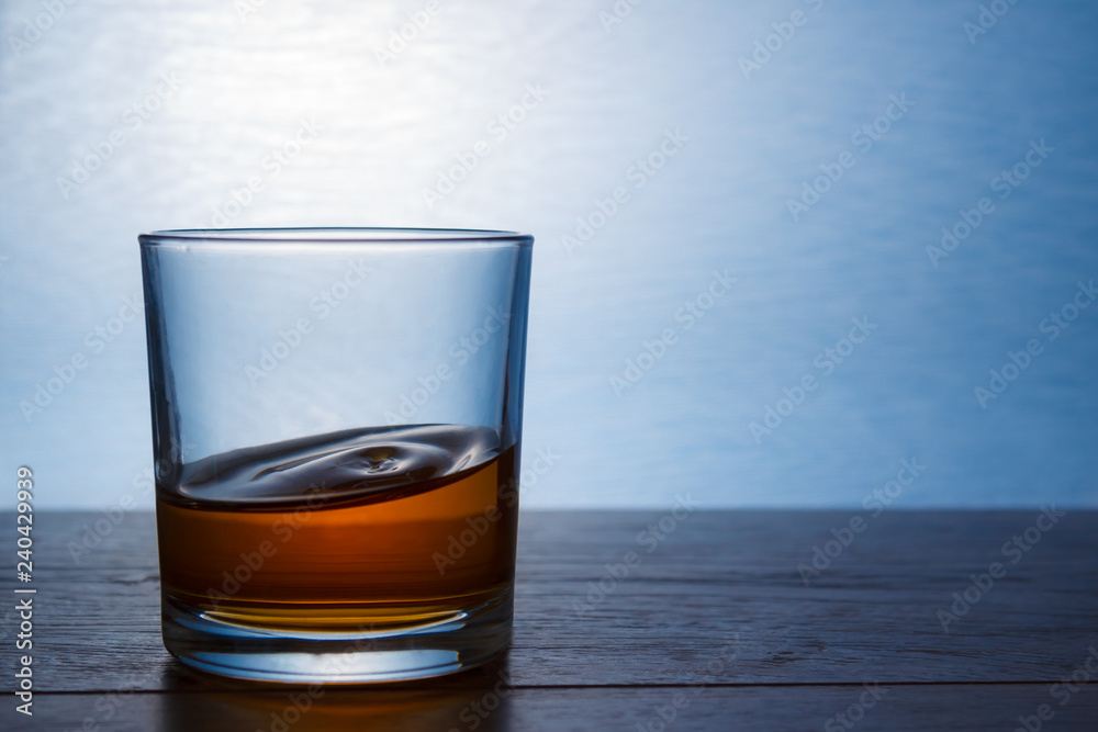 A glass of whiskey stands on a wooden table in backlight A glass of whiskey stands on a wooden table in backlight