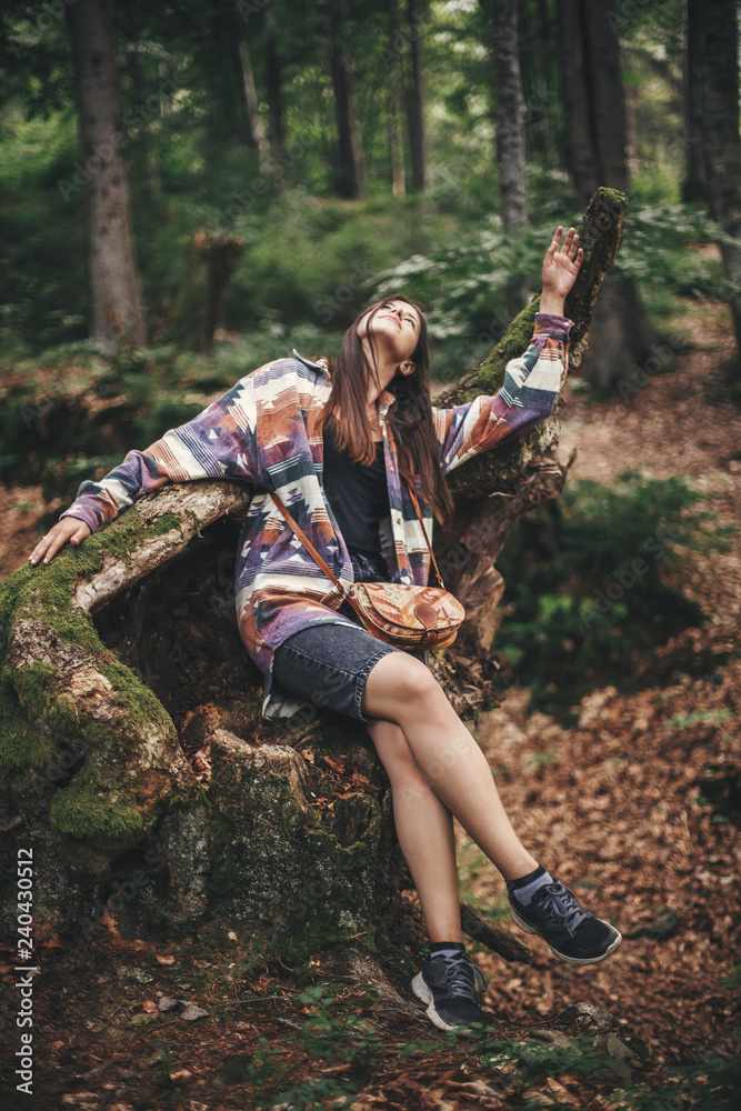 Stylish hipster girl having fun and relaxing in forest in mountains. Young woman traveler exploring woods. Eco holiday. Travel and wanderlust. Funny moment