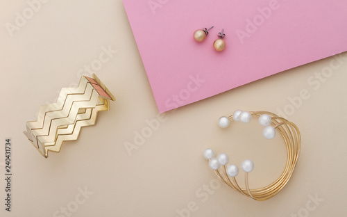 Golden and pearls bracelet and golden cuff with pair of earrings on pink and beige