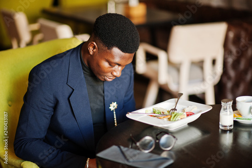 Fashionable african american man in suit sitting at cafe and looking on phone.
