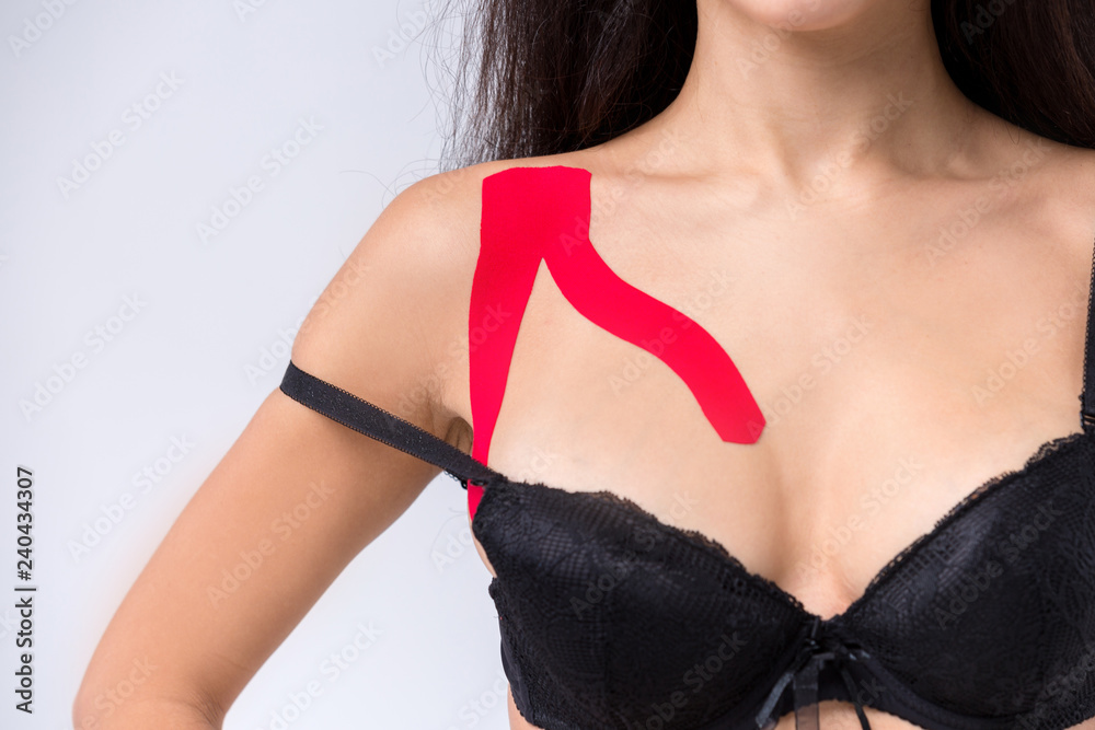 The theme kinesiology taping, stretching, trauma and muscle pain. Close-up.  sexy caucasian woman with long brunette hair posing in black lingerie with  red lipstick tape on shoulder on isolated Stock Photo