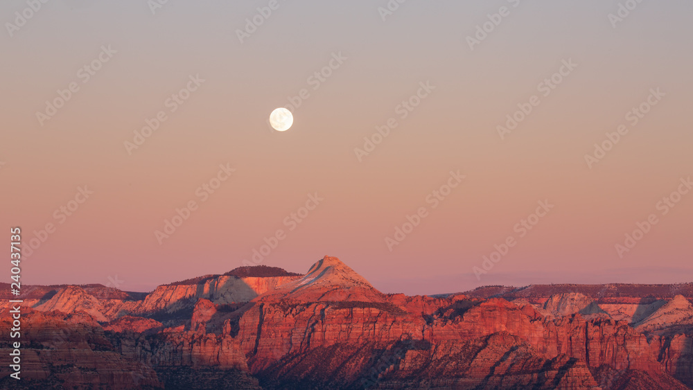 The full moon rises above the mountains of Zion national park as the last light of sunset touches the peaks on the evening of winter solstice. 