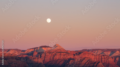 The full moon rises above the mountains of Zion national park as the last light of sunset touches the peaks on the evening of winter solstice. 