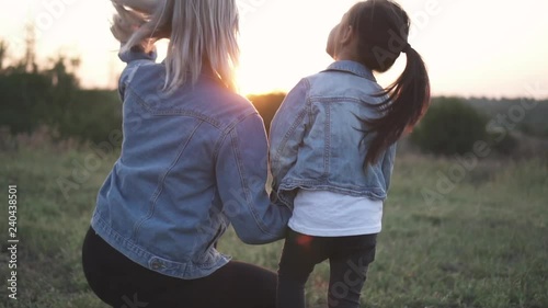 Mixed race family, european mother and asian daughter spending time in the park. Mother shows to her daughter how beautiful the sunset is. They both look at the sun shot frpm behind. Spring or summer photo