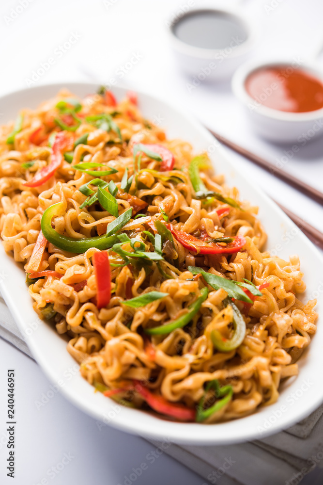 Schezwan veg noodles is a spicy and tasty stir fried flat Hakka noodles with sauce and veggies. served with chopsticks. selective focus