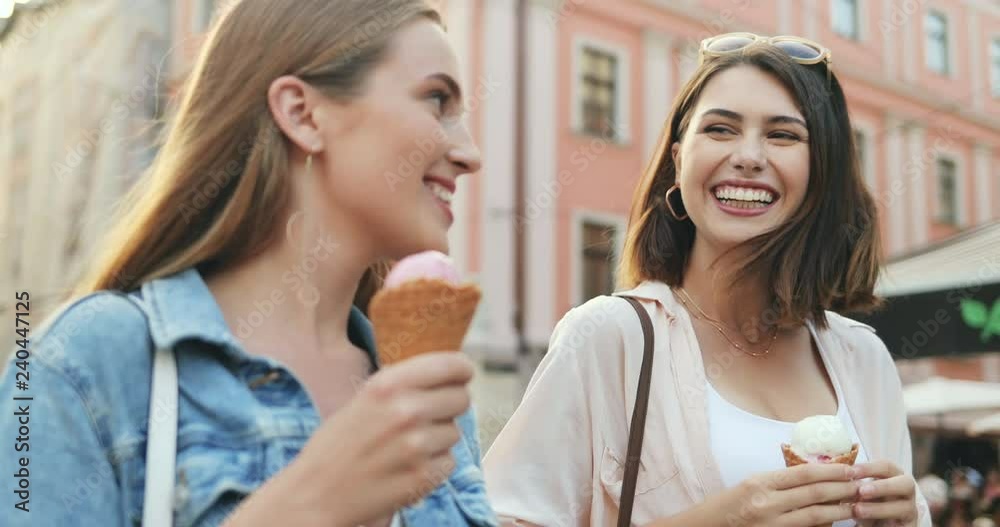 Close up of the two joyful young Caucasian women friends walking the city center, talking and eating ice-cream. Outdoors. Close up of the two joyful young Caucasian women friends walking the city center, talking and eating ice-cream. Outdoors.