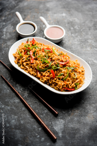 Schezwan veg noodles is a spicy and tasty stir fried flat Hakka noodles with sauce and veggies. served with chopsticks. selective focus