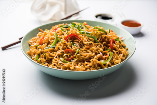 Schezwan veg noodles is a spicy and tasty stir fried flat Hakka noodles with sauce and veggies. served with chopsticks. selective focus photo
