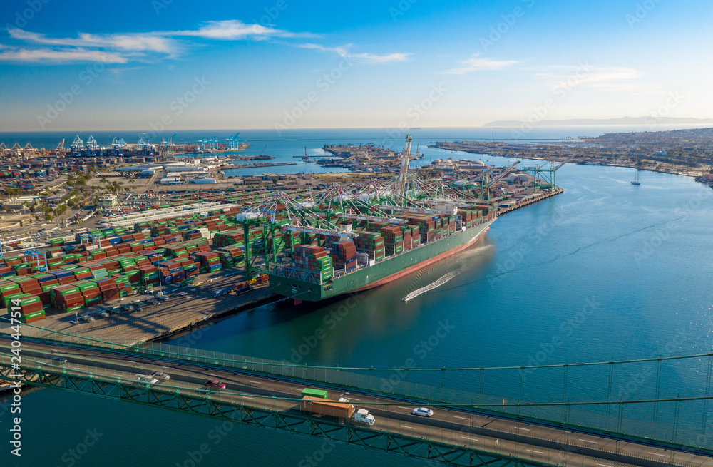 Aerial view of harbor unloading cargo from a large container ship with cranes from above with transport bridge.