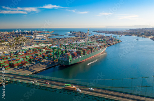 Aerial view of harbor unloading cargo from a large container ship with cranes from above with transport bridge. © Newport Coast Media
