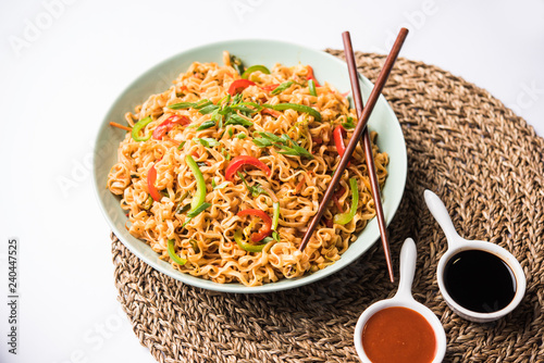 Schezwan veg noodles is a spicy and tasty stir fried flat Hakka noodles with sauce and veggies. served with chopsticks. selective focus photo