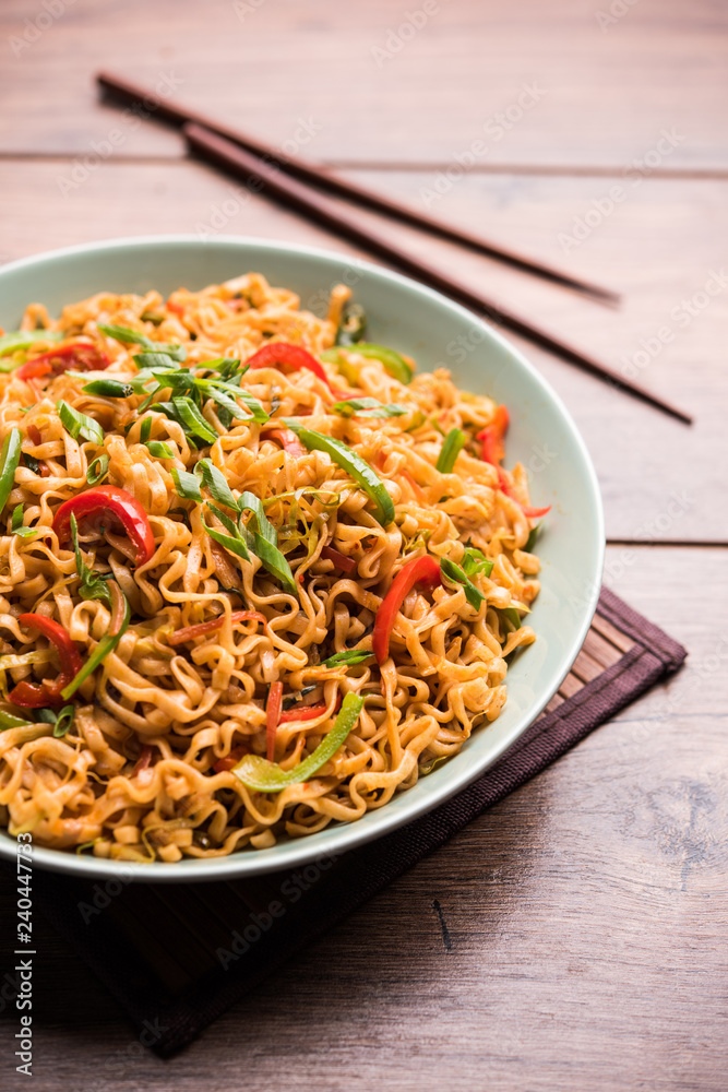 Schezwan veg noodles is a spicy and tasty stir fried flat Hakka noodles with sauce and veggies. served with chopsticks. selective focus Schezwan veg noodles is a spicy and tasty stir fried flat Hakka noodles with sauce and veggies. served with chopsticks. selective focus