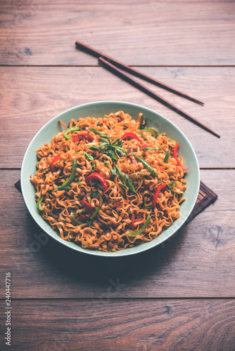 Schezwan veg noodles is a spicy and tasty stir fried flat Hakka noodles with sauce and veggies. served with chopsticks. selective focus photo