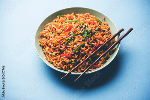 Schezwan veg noodles is a spicy and tasty stir fried flat Hakka noodles with sauce and veggies. served with chopsticks. selective focus photo