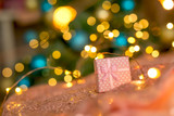 Pink gift on a coral background against a blurred New Year tree .