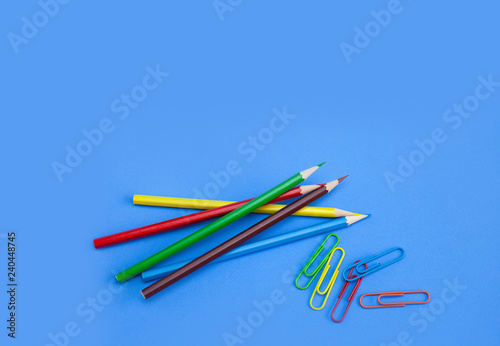 Stationery office supplies concept, Colored crayon pencils with colorful clips on blue background with copy space. Top view.