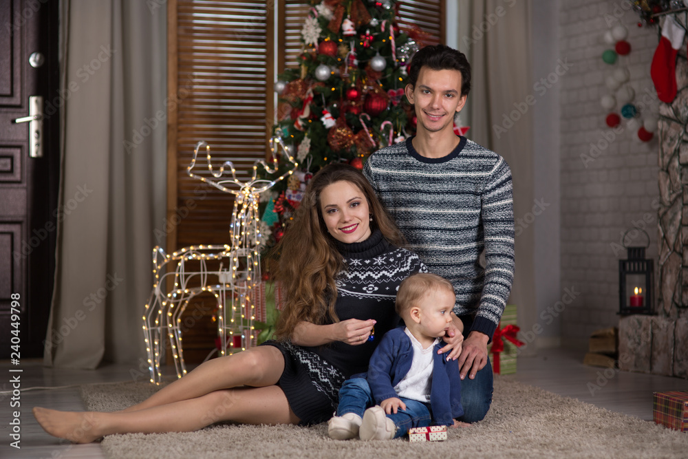 family sits with the baby sitting near the Christmas tree, family sits with the baby sitting near the Christmas tree,