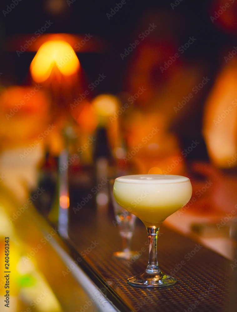 White Cocktail drink-beverage on  a bar.  Selective focus on the foreground glass,night background . Blurred people in the background.  Trendy black stylish  edit. Copy paste space for design concept