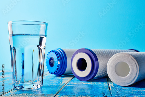 Water filters. Carbon cartridges and a glass on a blue background. Household filtration system.
