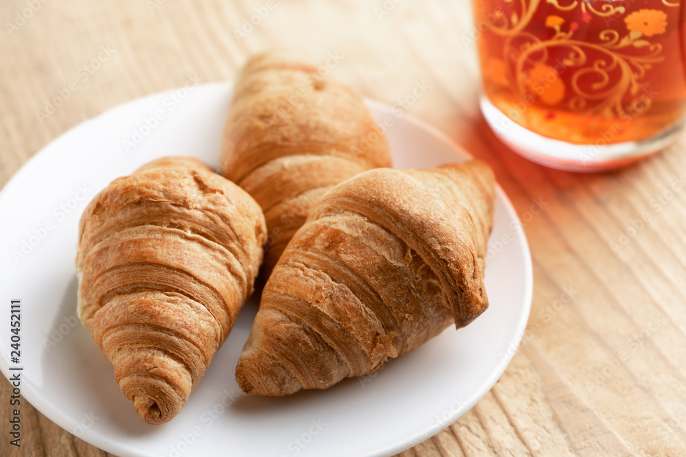 Three croissants on a white plate next to a Cup of tea