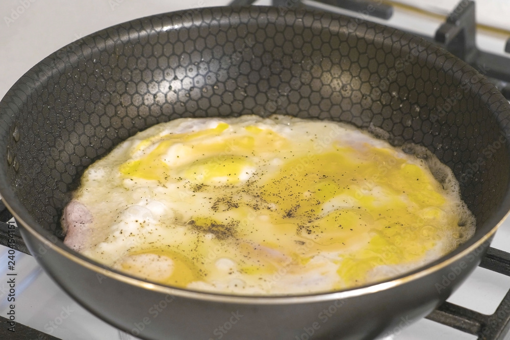 Preparing scrambled eggs with sausage in a frying pan on gas stove.