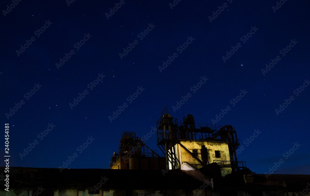 Built on sunset background. Small plant against the night sky. Starry sky over the plant. Silhouette of buildings against the dark sky. Built on sunset background. Small plant against the night sky. Starry sky over the plant. Silhouette of buildings against the dark sky.