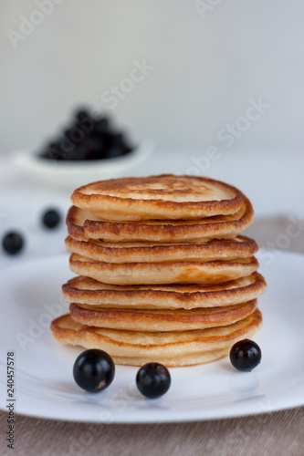 Stack of american pancakes and fresh blackcurrant are lying on a white plate.