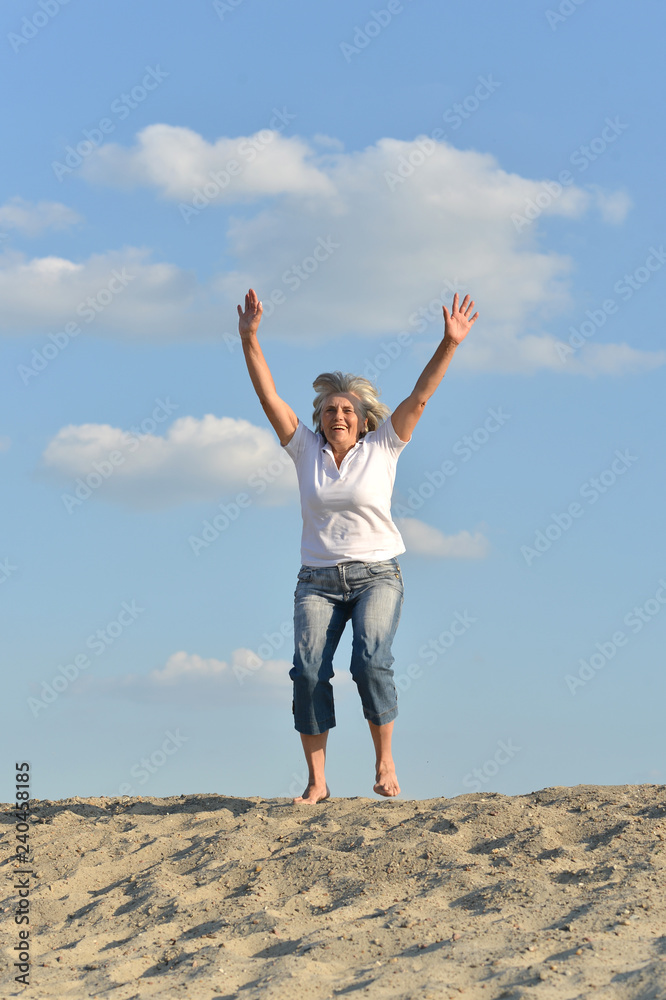 Portrait of happy senior woman jumping on sandy hill Portrait of happy senior woman jumping on sandy hill