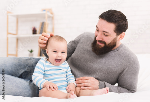Young bearded man playing with his little baby in bed