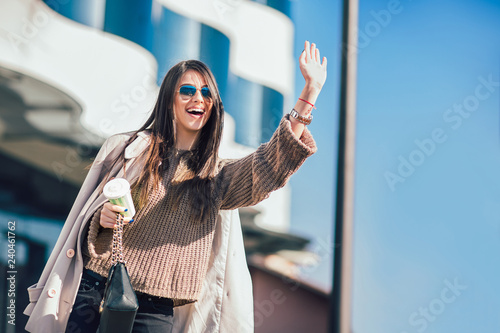 Young attractive busy businesswoman calling taxi, outdoor shoot with blurred buildings and street as background