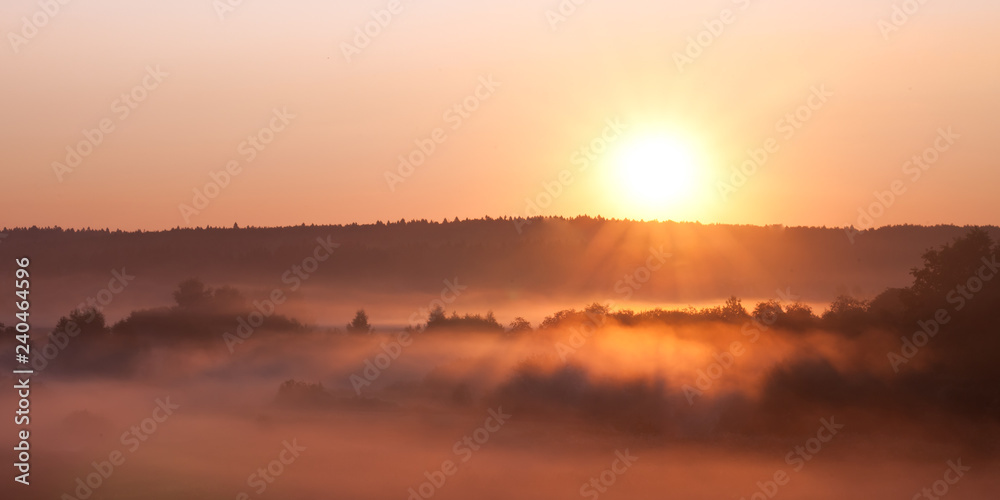 the hot sun rises over the misty valley.
