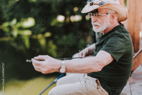 Nice elderly bearded angler holding a rod while fishing on the weekend
