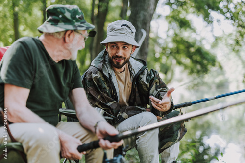 Pleasant man talking with his son while fishing