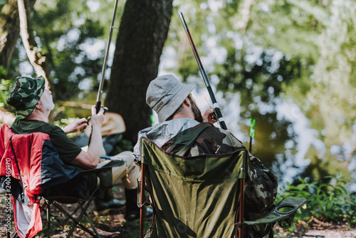 Rear view of delighted men enjoying fishing on the river bank